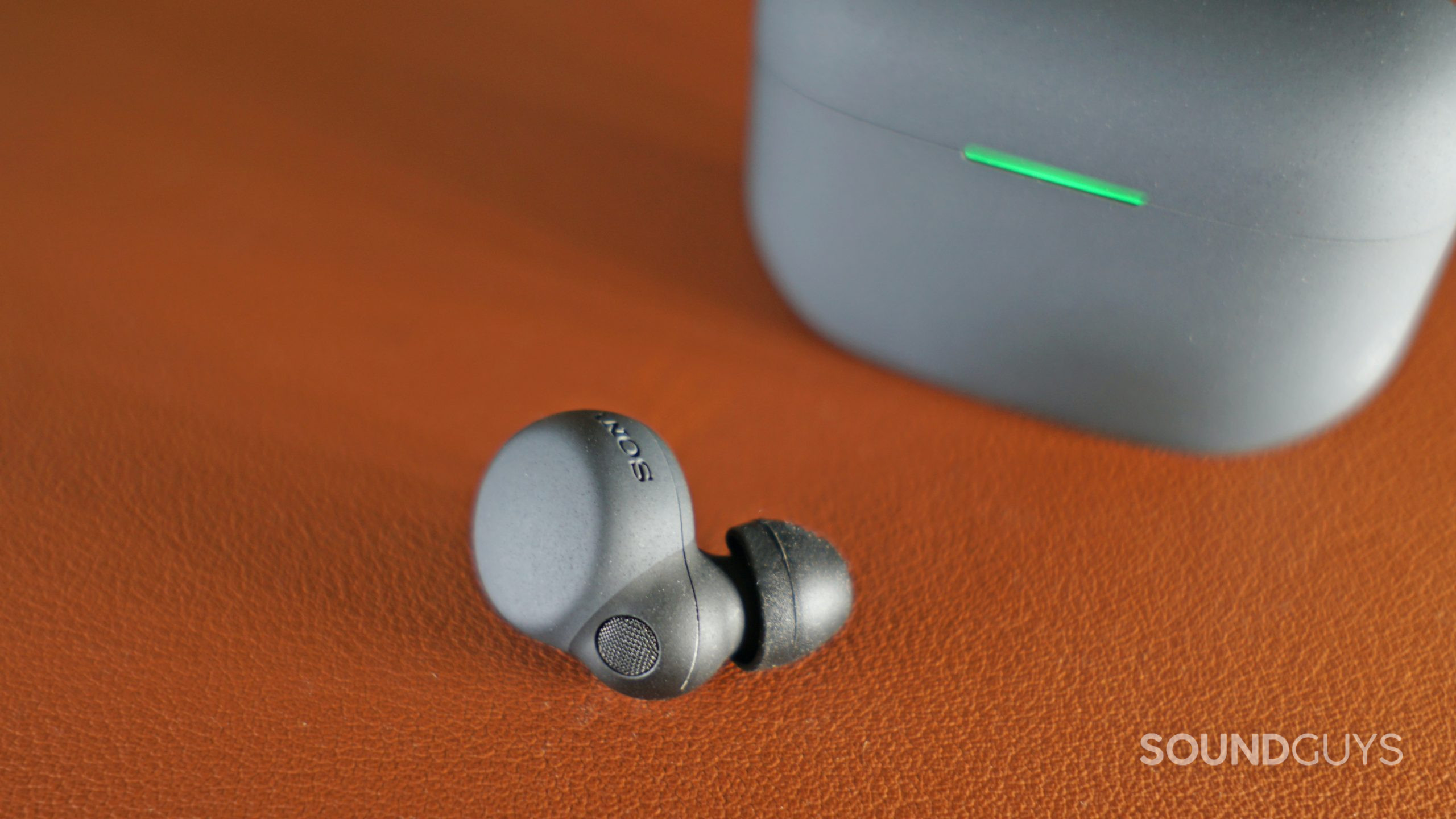 Sony-LinkBuds-S-closeup-bud The Sonly LinkBuds S earbud lays on a leather surface in front of its charging case.