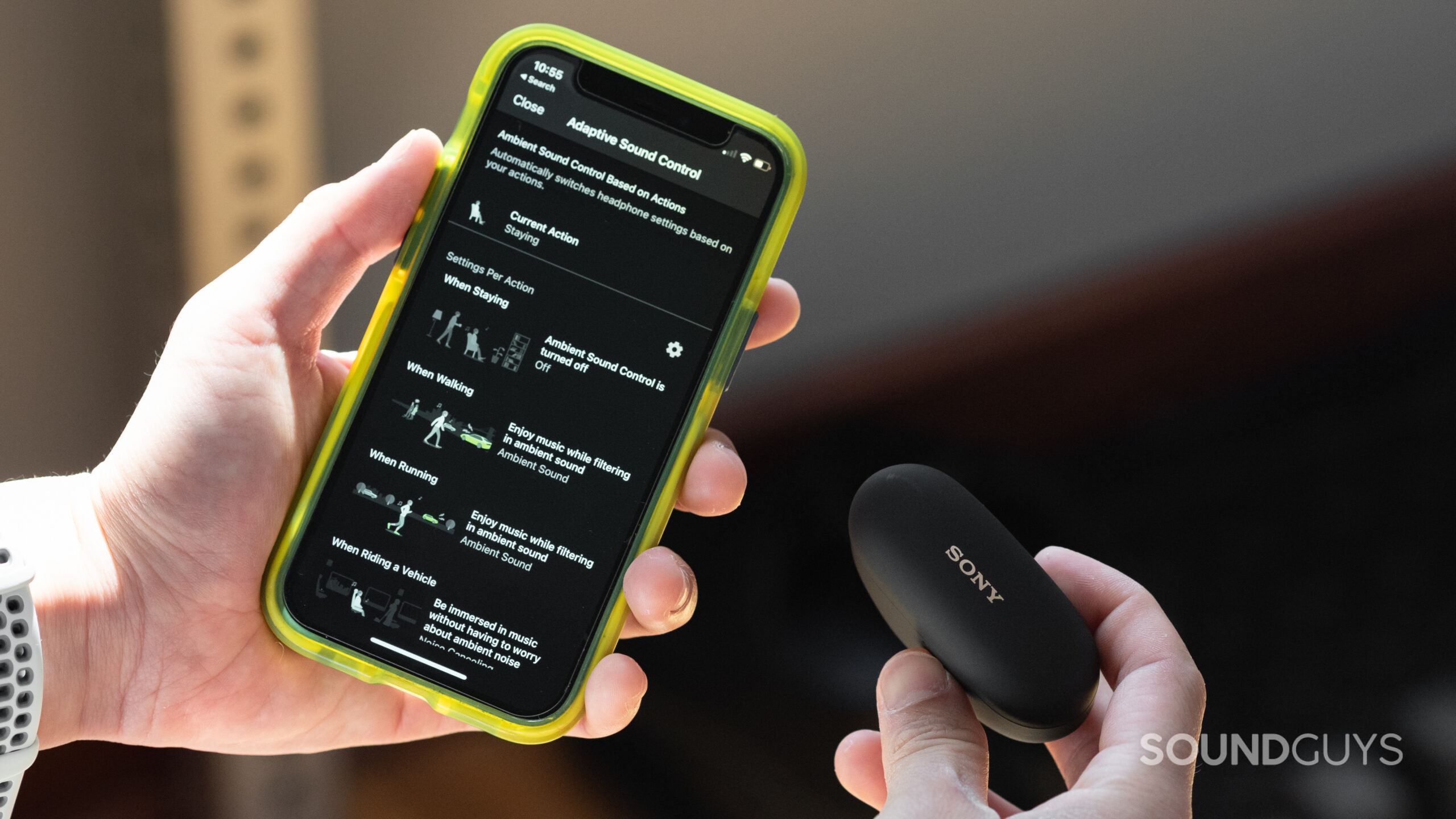 Sony WF-1000XM5 Headphones Connect app Adaptive Sound Control-1 Hands hold the Sony WF-1000XM5 and an iPhone displaying the Adaptive Sound Control Settings in the Headphone Connect app.
