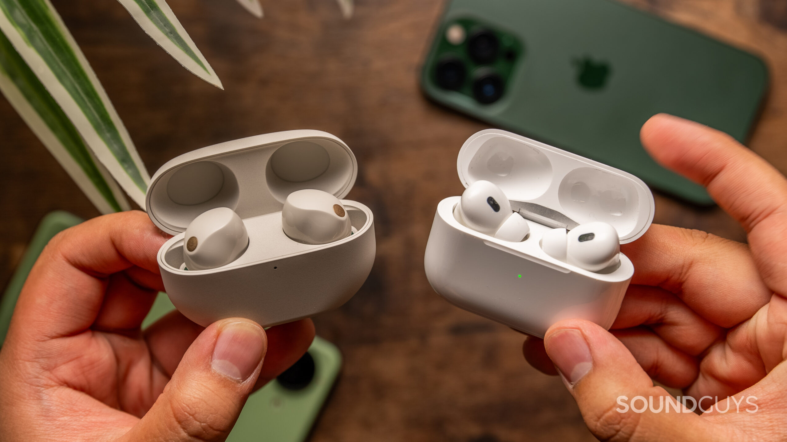 Sony WF-1000XM5 vs Apple AirPods Pro 2nd generation hands hold comparison A hand holds the Sony WF-1000XM5 and Apple AirPods Pro 2 cases in each hand.
