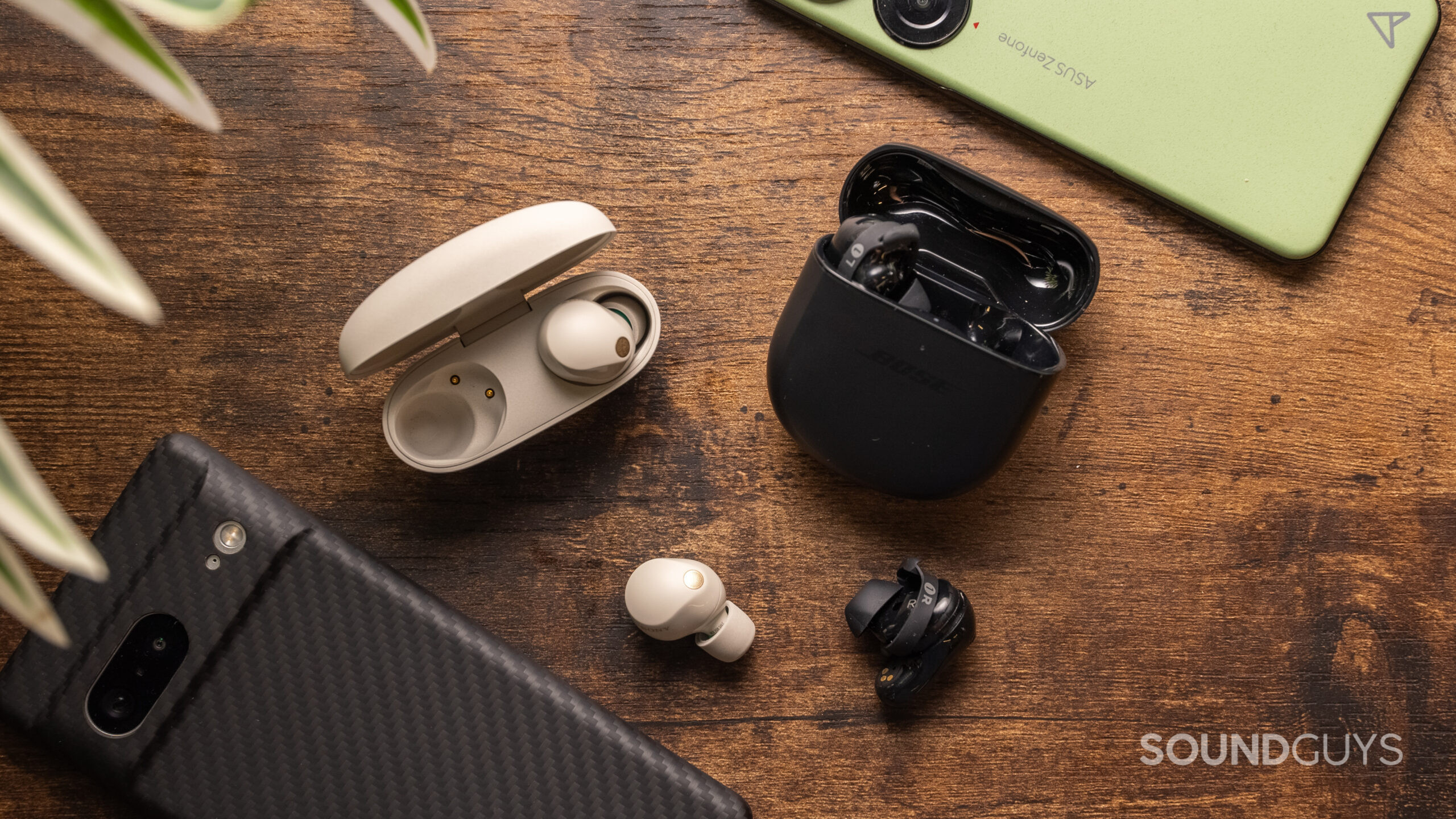 Sony WF-1000XM5 vs Bose QuietComfort Earbuds 2 one earbud outside charging case The Sony WF-1000XM5 and the Bose QuietComfort Earbuds II sitting side by side on a wooden table.