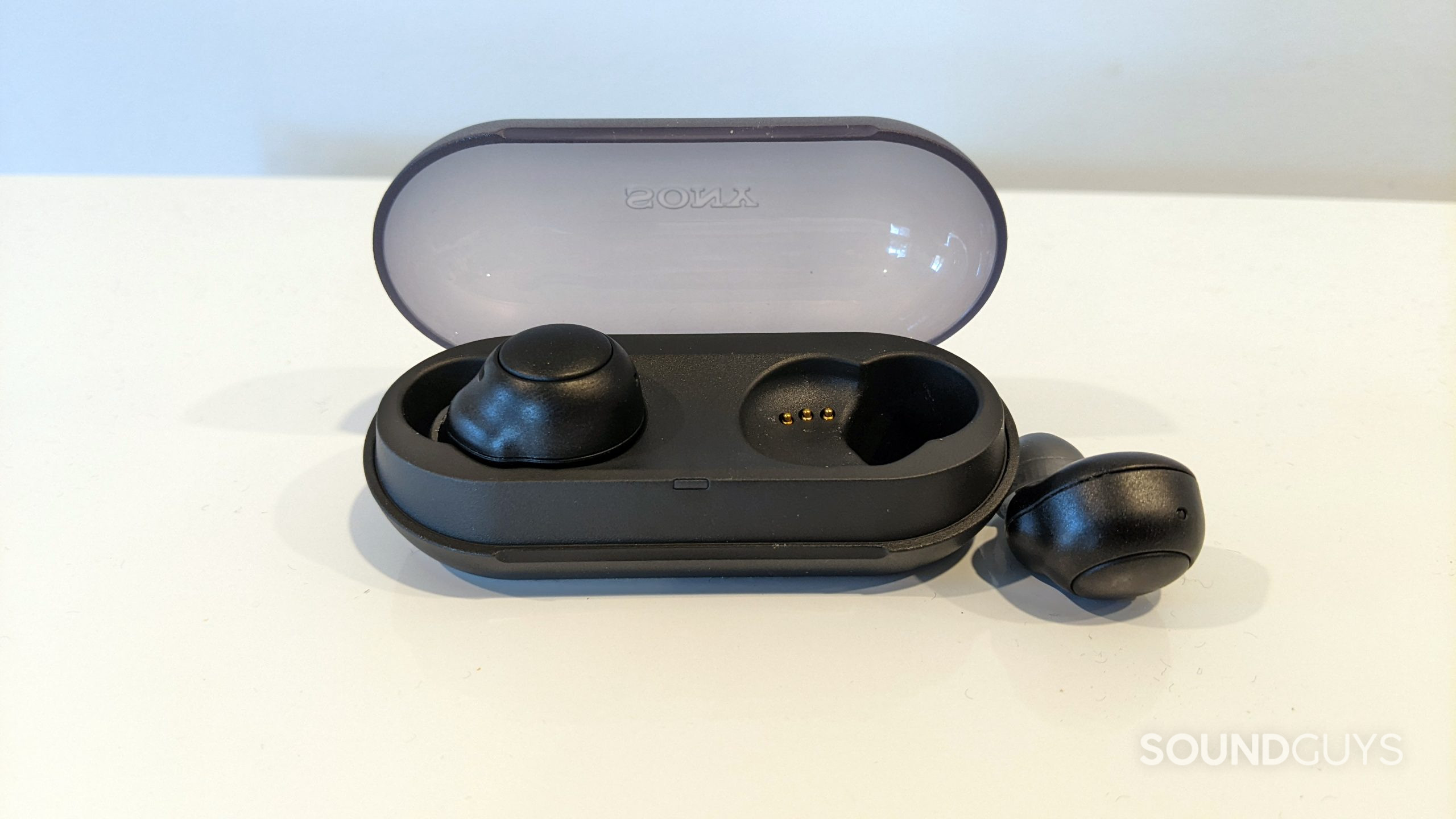 sony-wf-c500-one-out-of-case The Sony WF-C500 casewith the left earbud inside of it and the right one lying next to it on a white surface.
