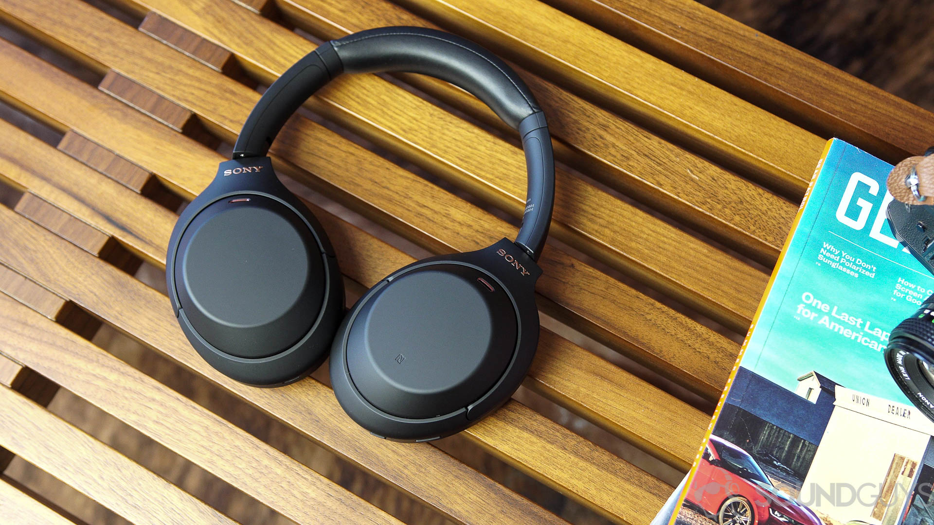 Sony WH-1000XM4 lying flat Sony WH-1000XM4 headphones next to magazines on a wood bench