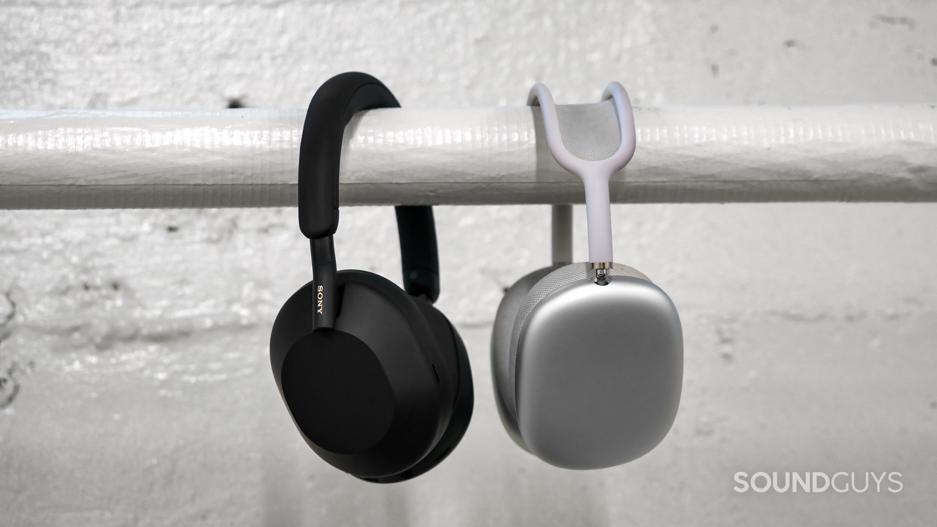 sony-wh-1000xm5-vs-apple-airpods-max Side-on view of Sony WH-1000XM5 beside the AirPods Max hanging over a white horizontal pipe