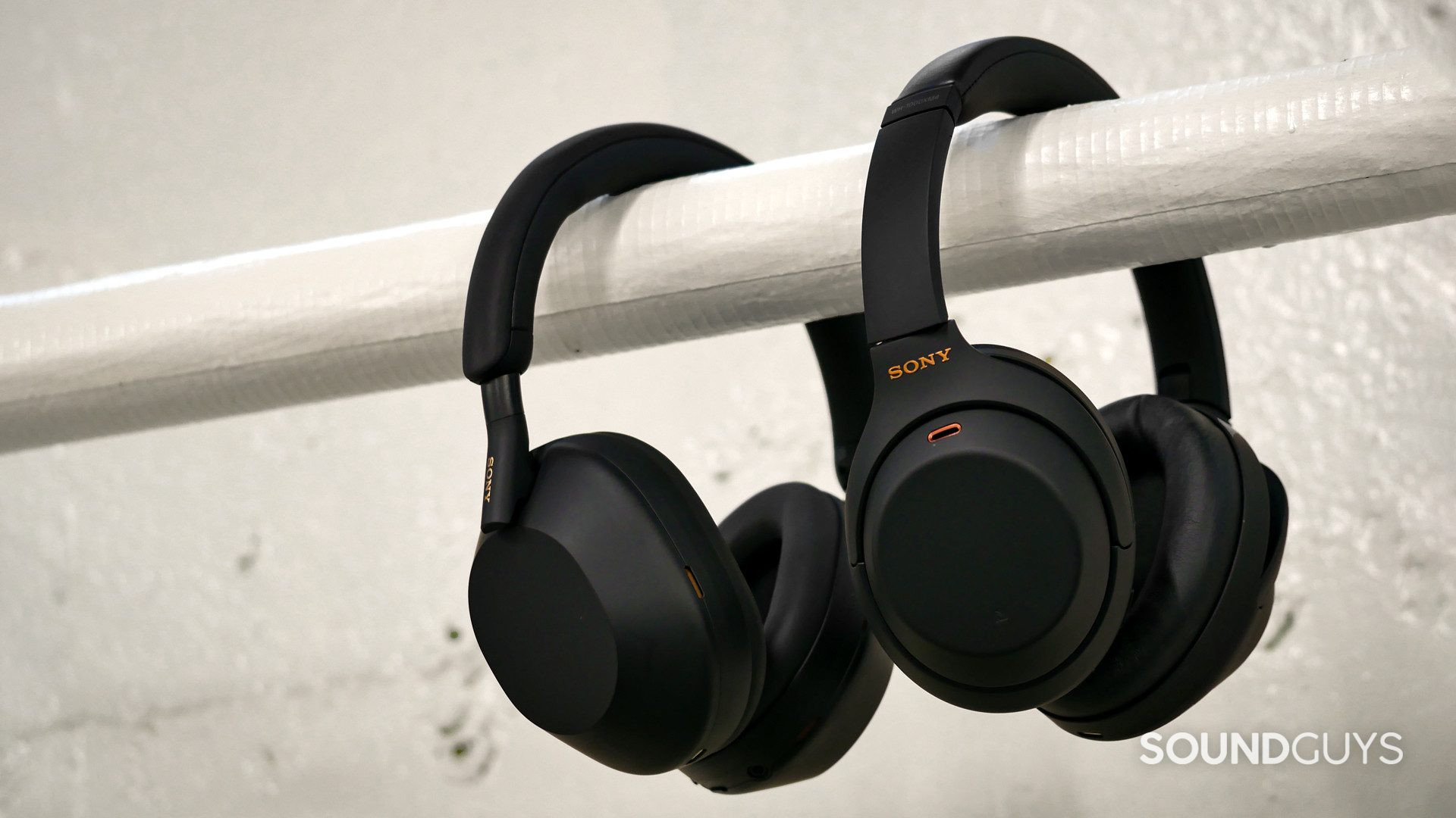 sony-wh-1000xm5-vs-sony-wh-1000xm4 Side-on view of Sony WH-1000XM5 beside the Sony WH-1000XM4 hanging over a white horizontal pipe