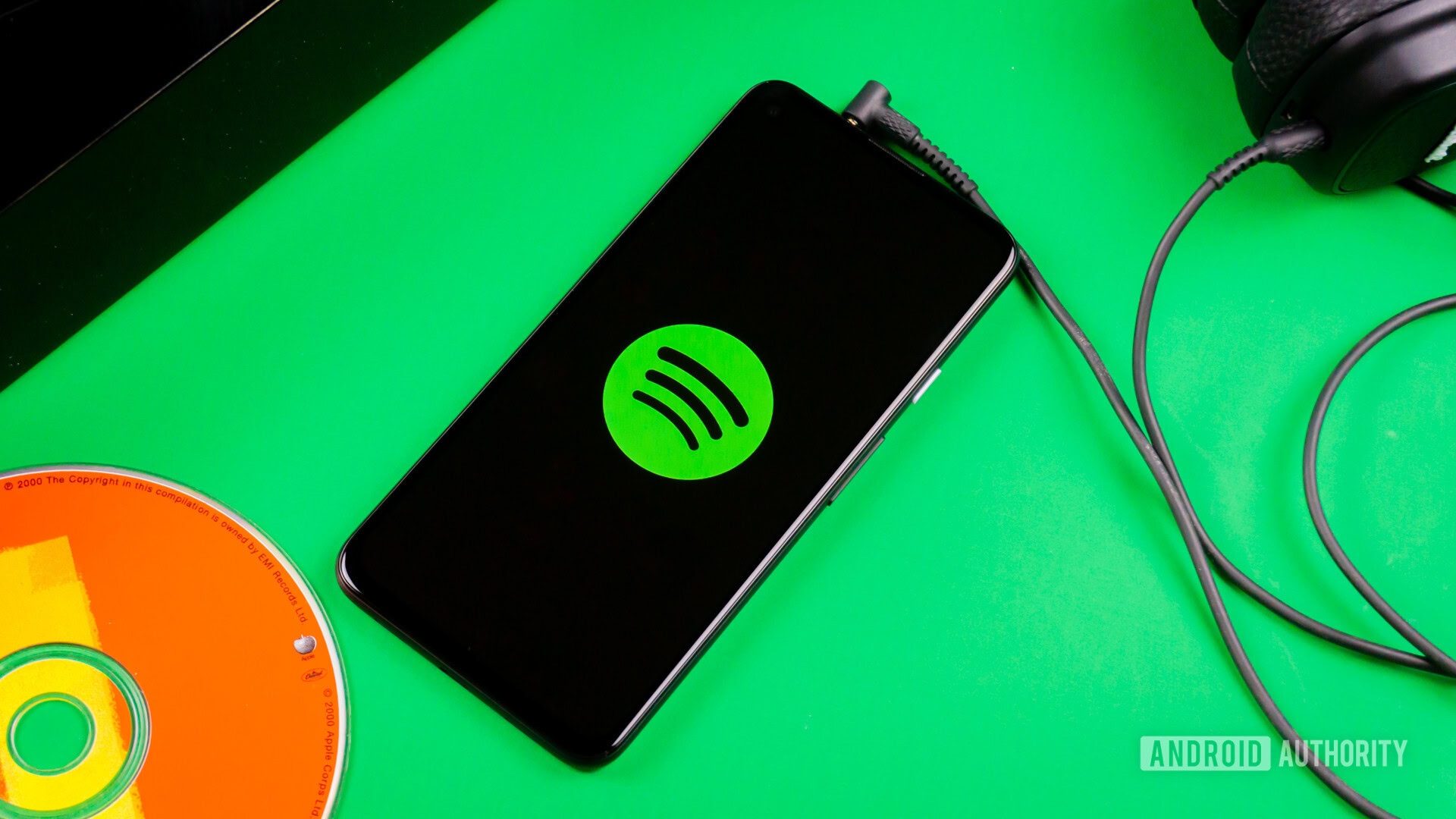 Spotify1 A phone sits on a green background, plugged into a set of wired earbuds. On the screen is the Spotify logo.