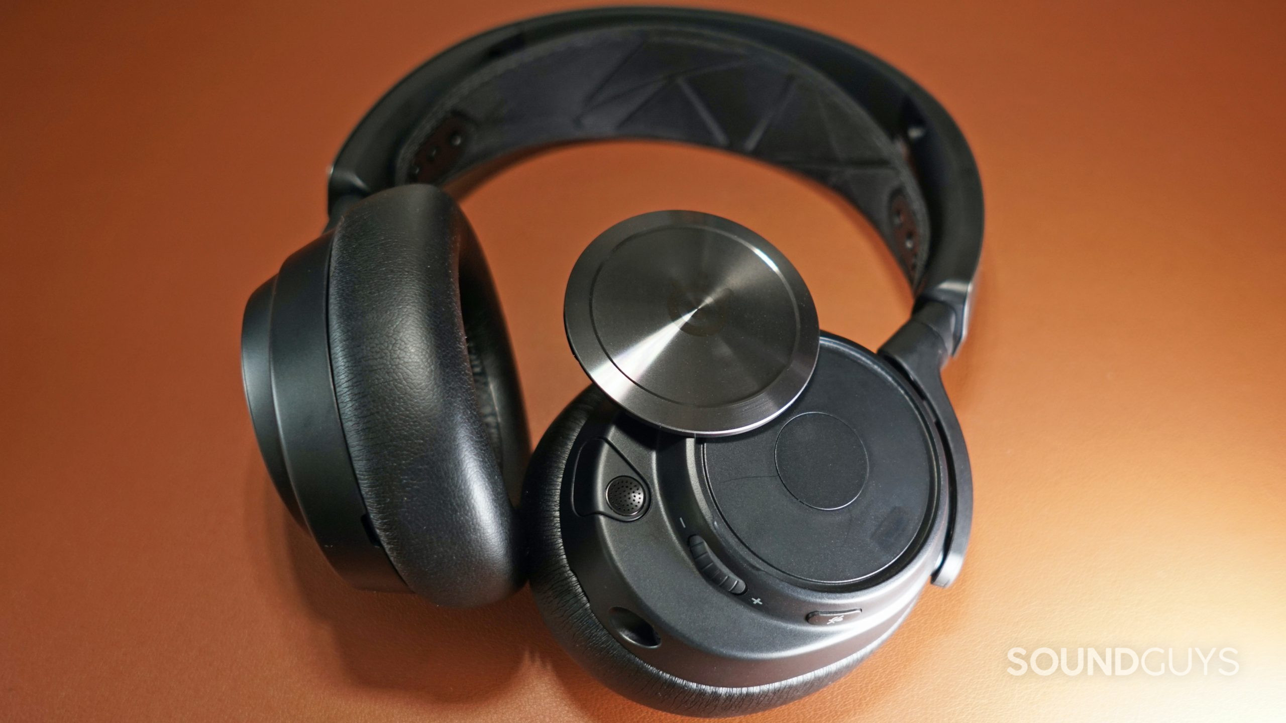 SteelSeries-Arctis-Nova-Pro-side-plate The SteelSeries Arctis Nova Pro lays on a leather surface, with one of its magnetic face plates partially detached,