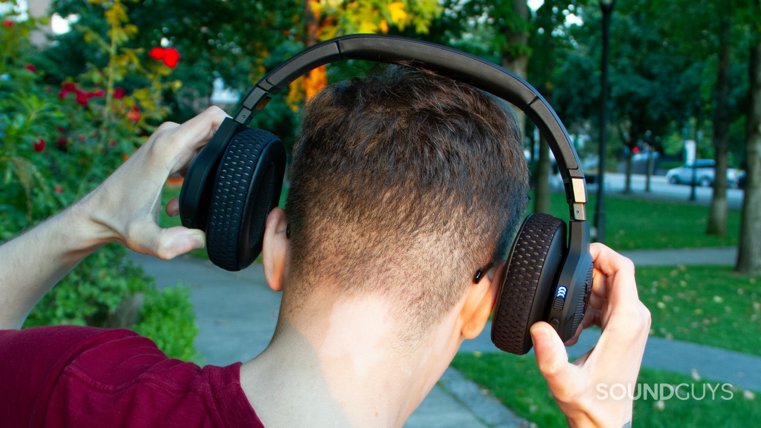 ua-jbl-project-rock-outside The back of Under Armour Project Rock by JBL headphones is shown being stretched out over the back of a man's head, about to put it on.