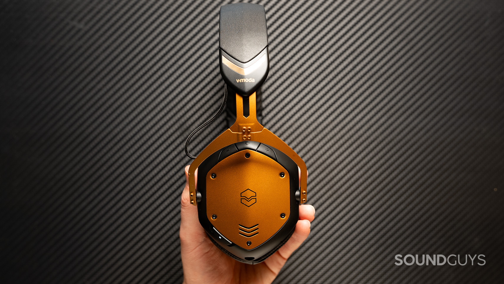 V-moda Crossfade 3 Wireless carbon background A hand holds the V-MODA Crossfade 3 Wireless with the buttons facing out.
