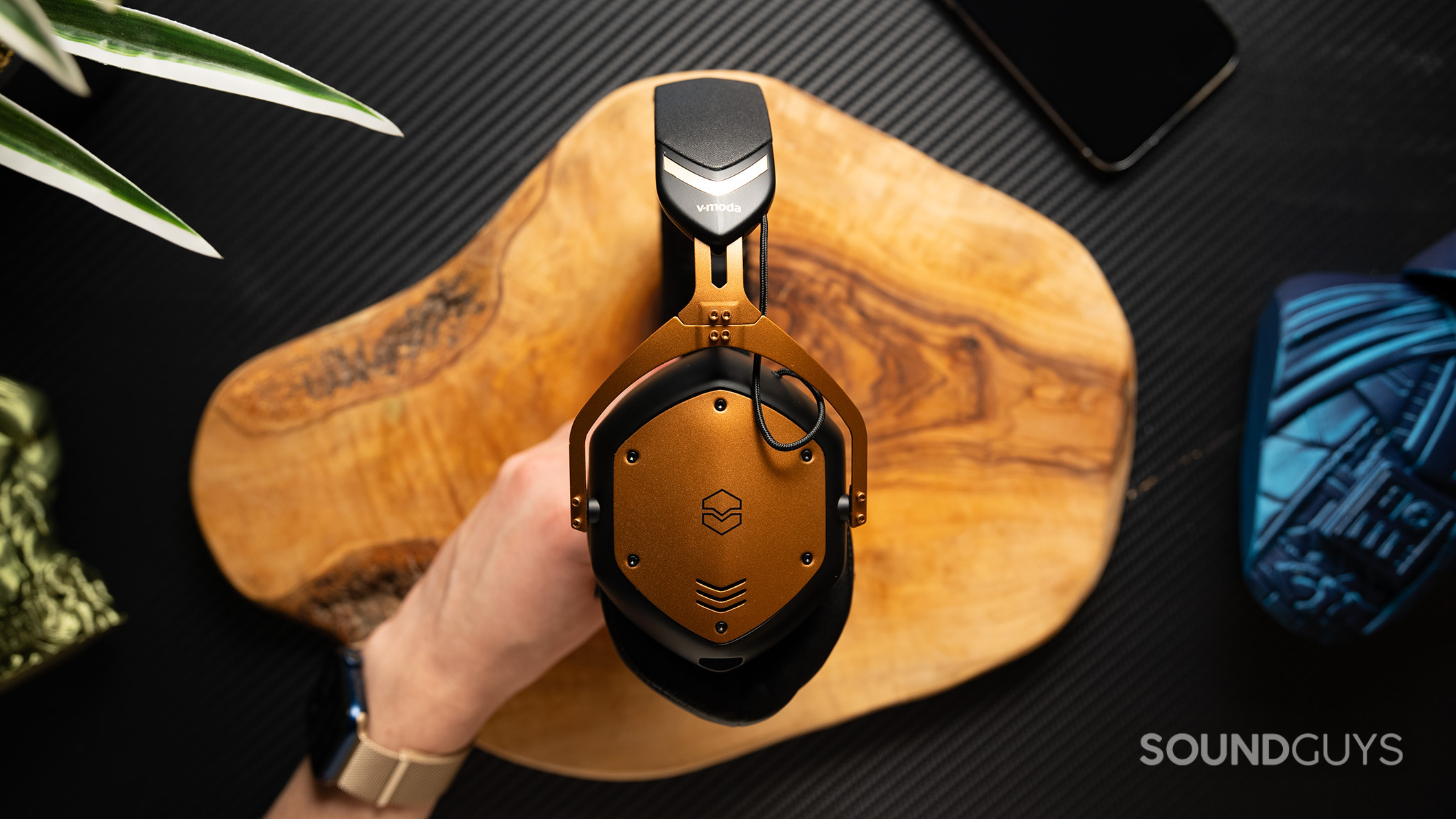 V-moda Crossfade 3 Wireless hero A hand holding the V-MODA Crossfade 3 Wireless headphones over a table.